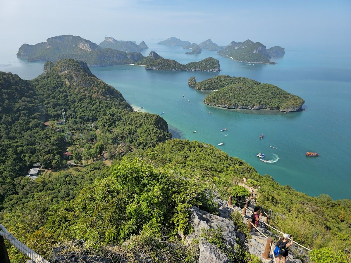 View from the Koh Wua Talap viewpoint in Ang Thong National Marine Park, showing the scattered limestone islands and turquoise water of the archipelago, with tourists on the rocky trail in the foreground
