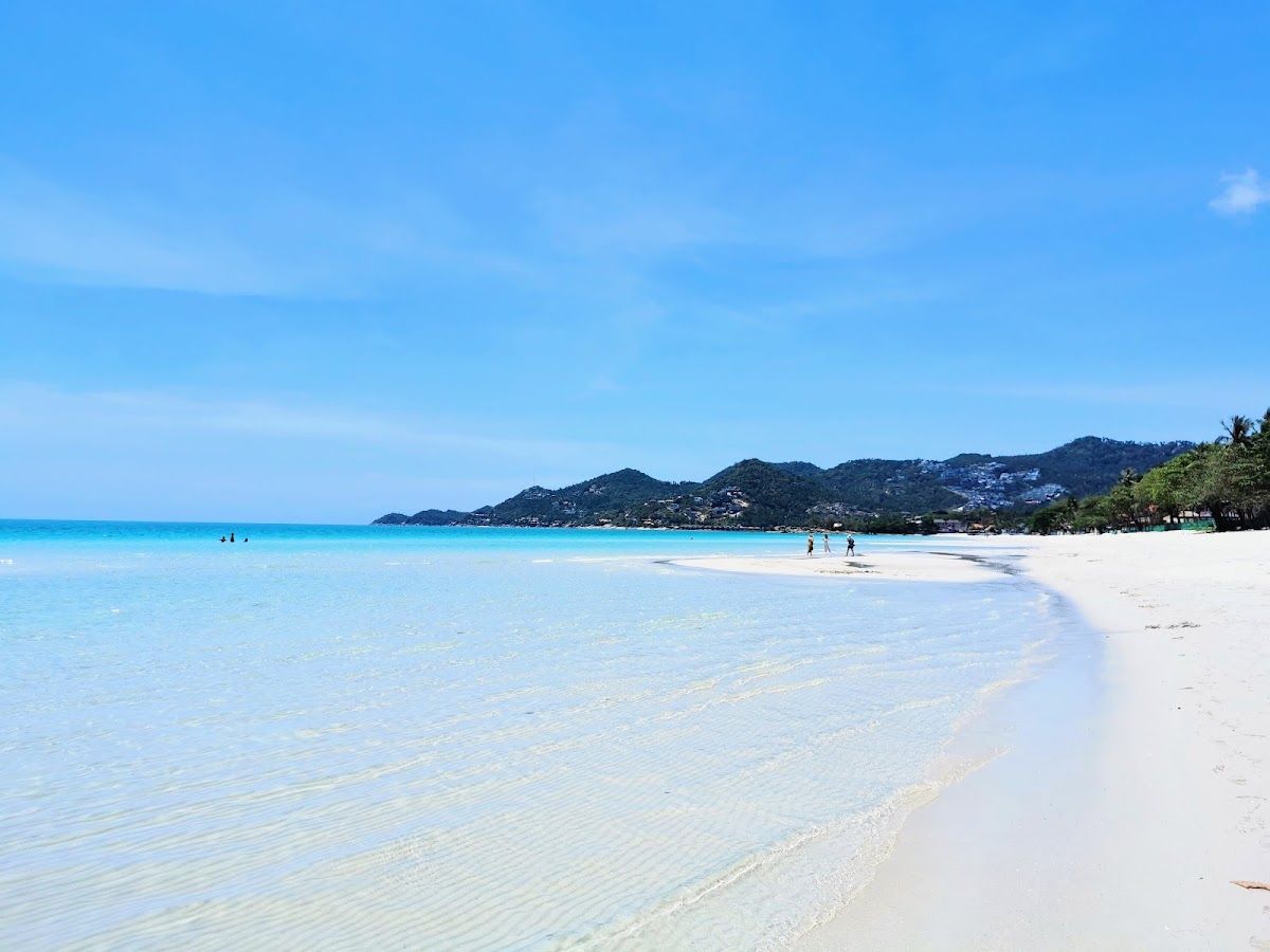 Chaweng Beach, Koh Samui — long stretch of white sand with clear turquoise water, sunbeds along the shore and green hills rising behind the beachfront hotels