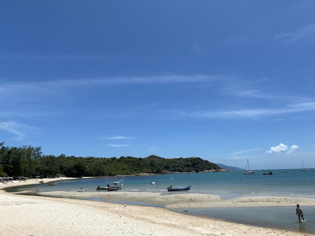 Choeng Mon Beach on Koh Samui with white sand, calm turquoise water, long-tail boats, and a forested headland in the background